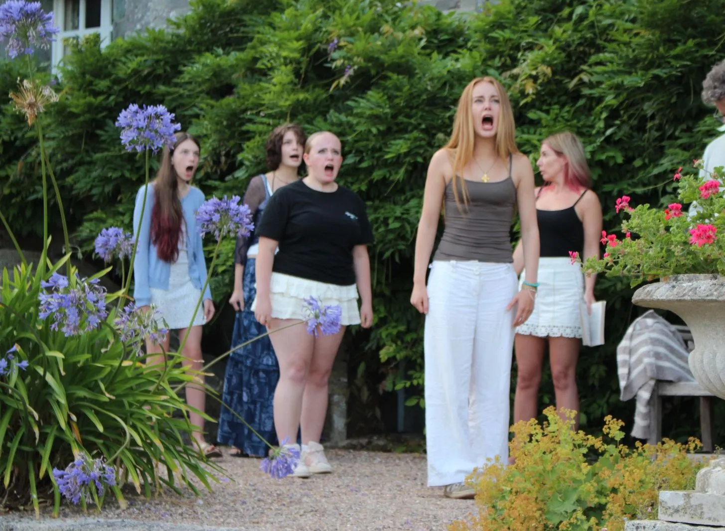 Cast members rehearsing an outdoor scene from The Crucible in a flower-filled garden.