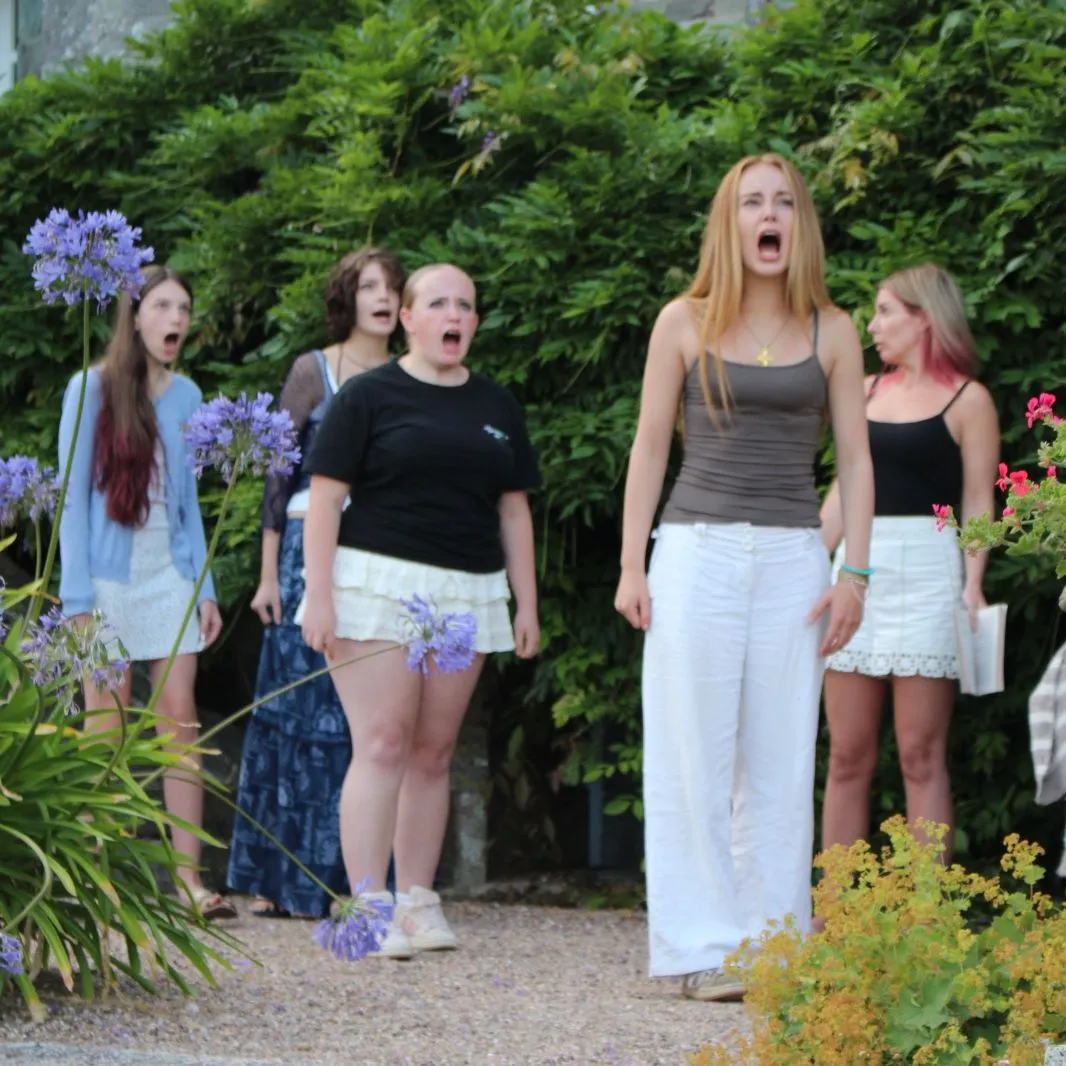 Cast members rehearsing an outdoor scene from The Crucible in a flower-filled garden.