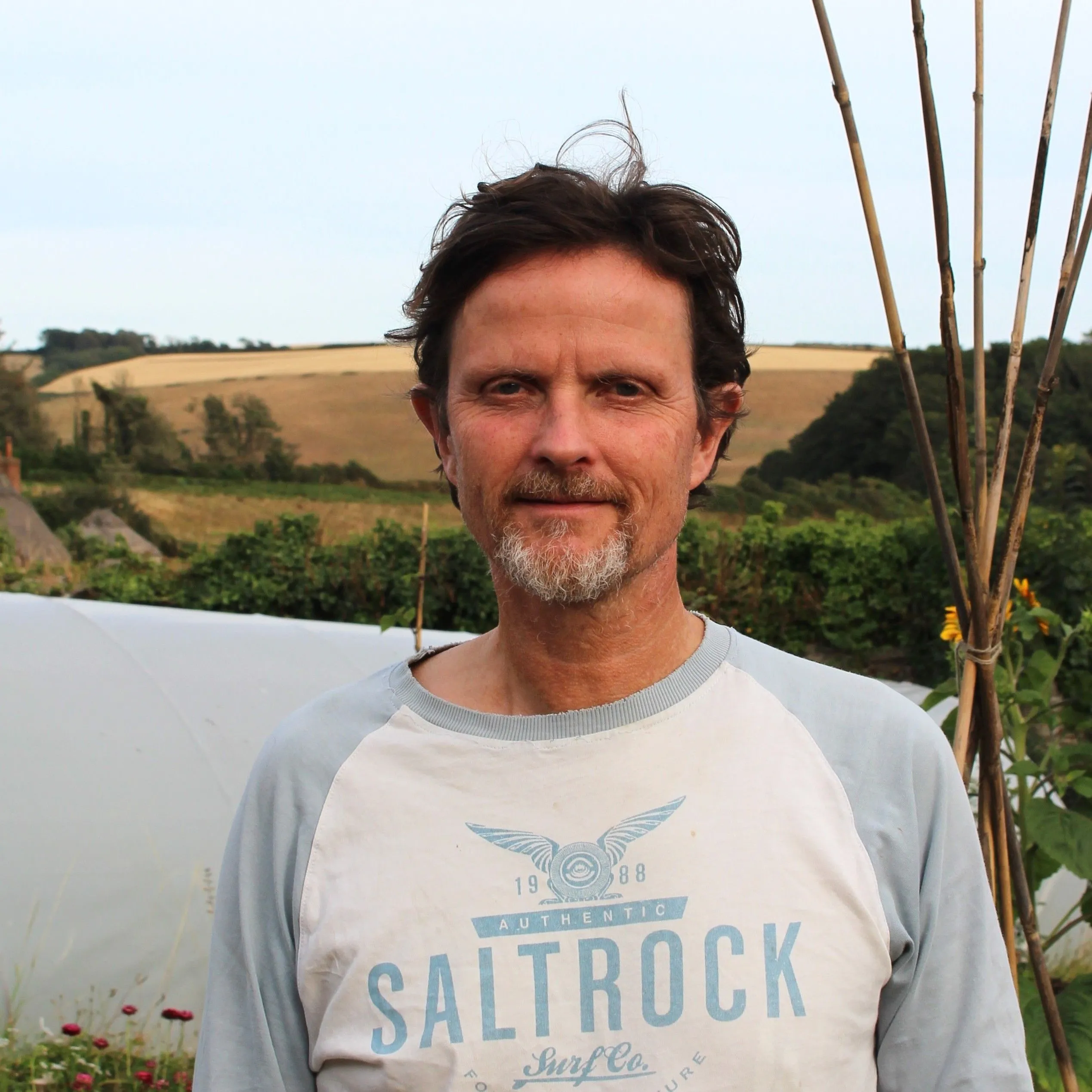 Portrait of Jonny Garstang standing in a market garden with rolling countryside behind him