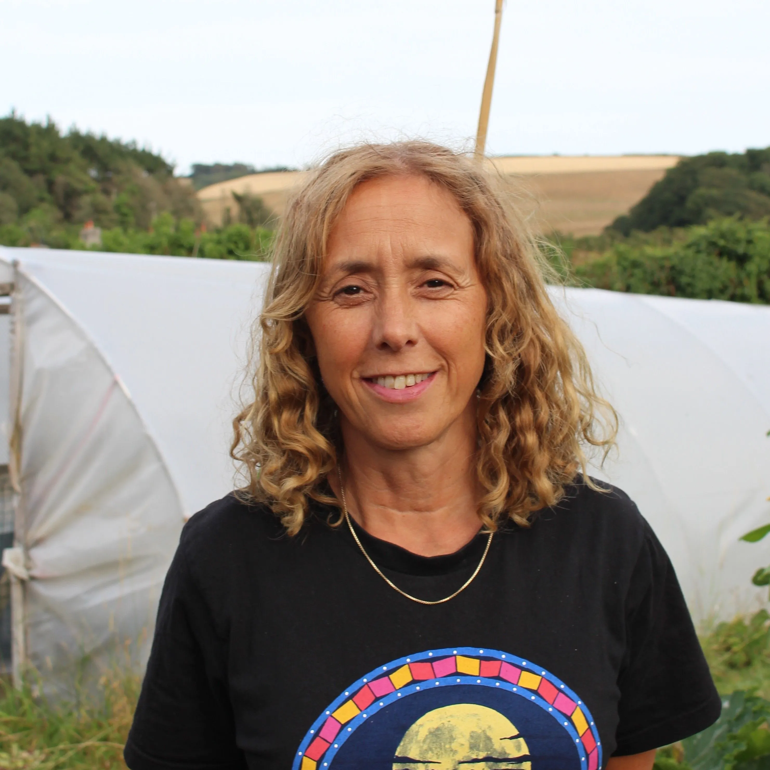 Portrait of Nell Carder smiling outdoors beside a polytunnel in the countryside.