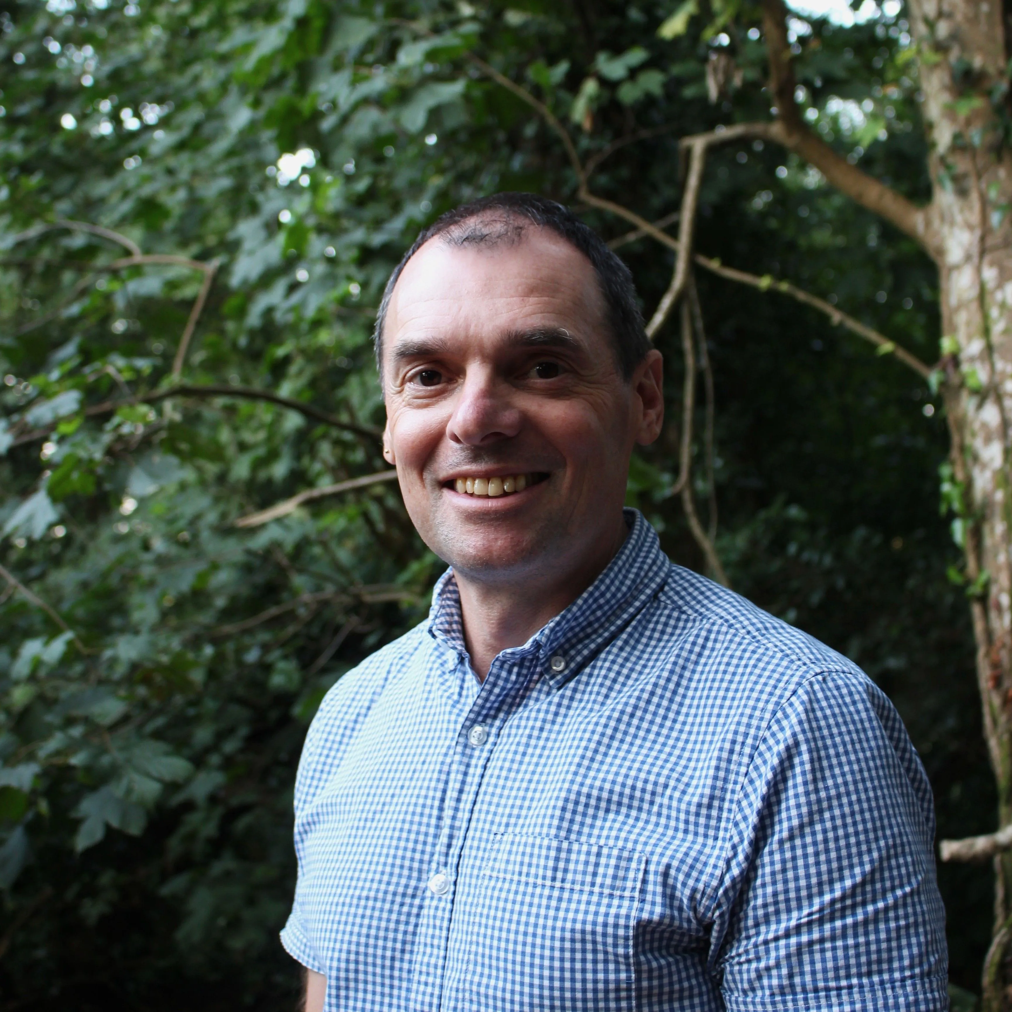 Portrait of Pete Stevens smiling outdoors beside leafy trees