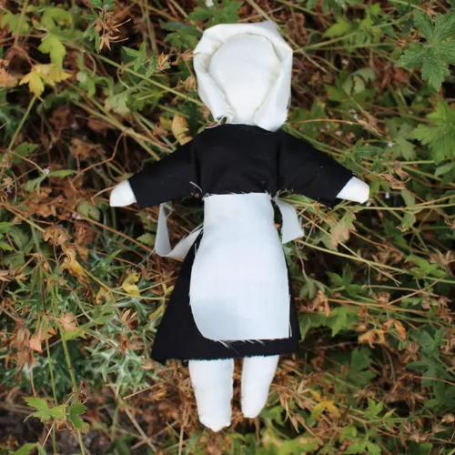 Handmade faceless cloth doll in a black dress with a white apron lying among wild plants