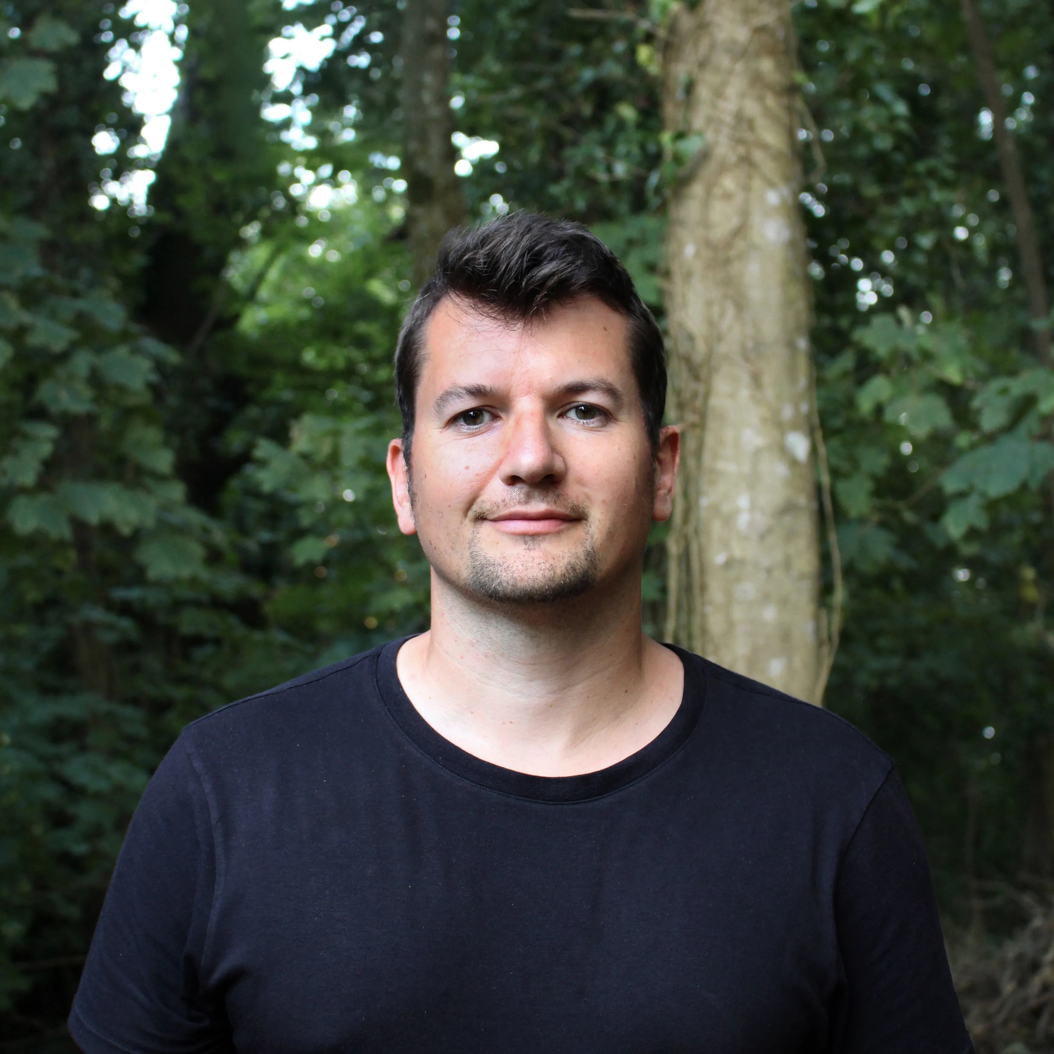 Portrait of Rob Currall standing outdoors in front of leafy trees.