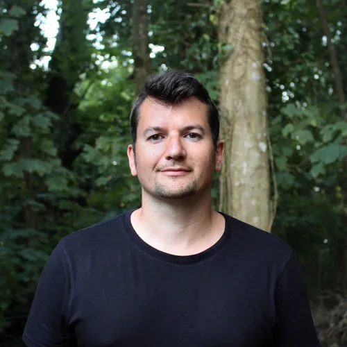 Portrait of Rob Currall standing outdoors in front of leafy trees.