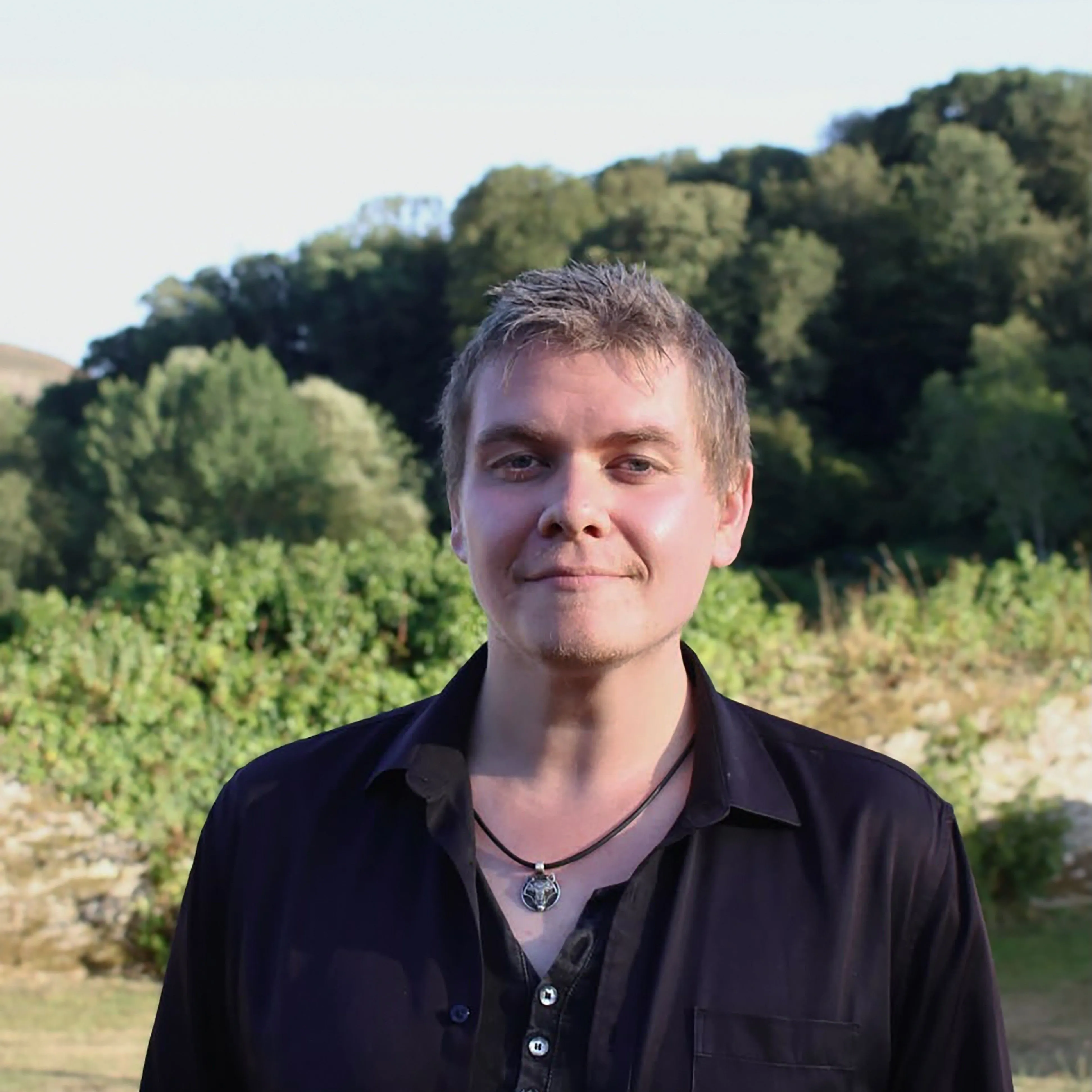 Portrait of John Currall standing outdoors before a wooded hillside