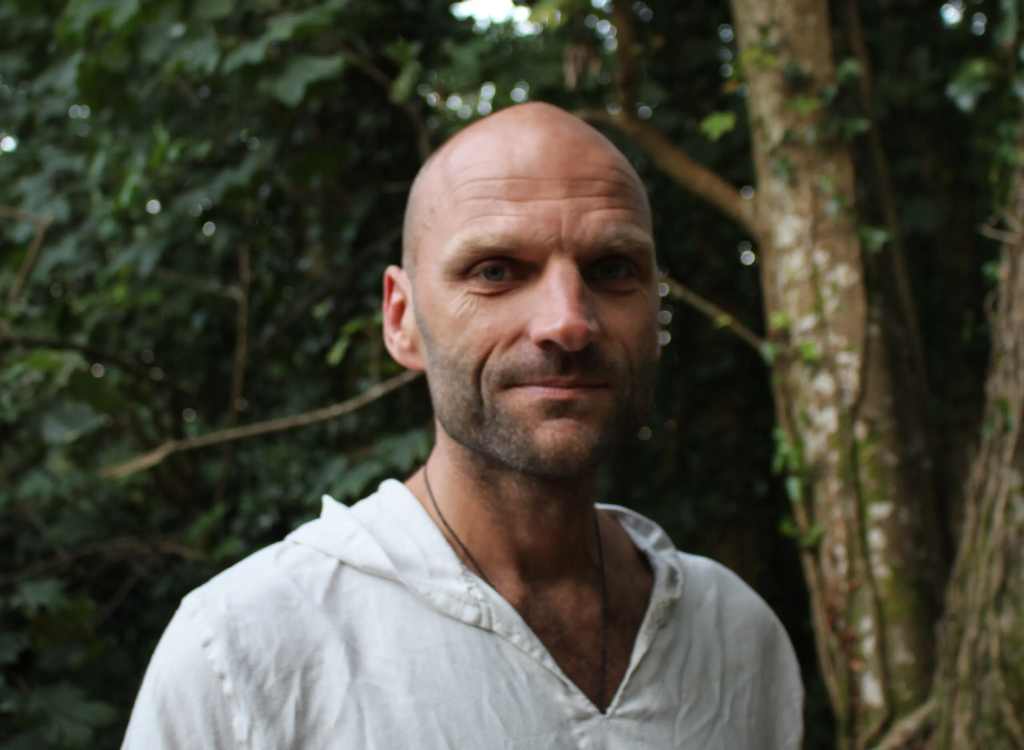 Portrait of John Honeybell wearing a white shirt in a leafy forest