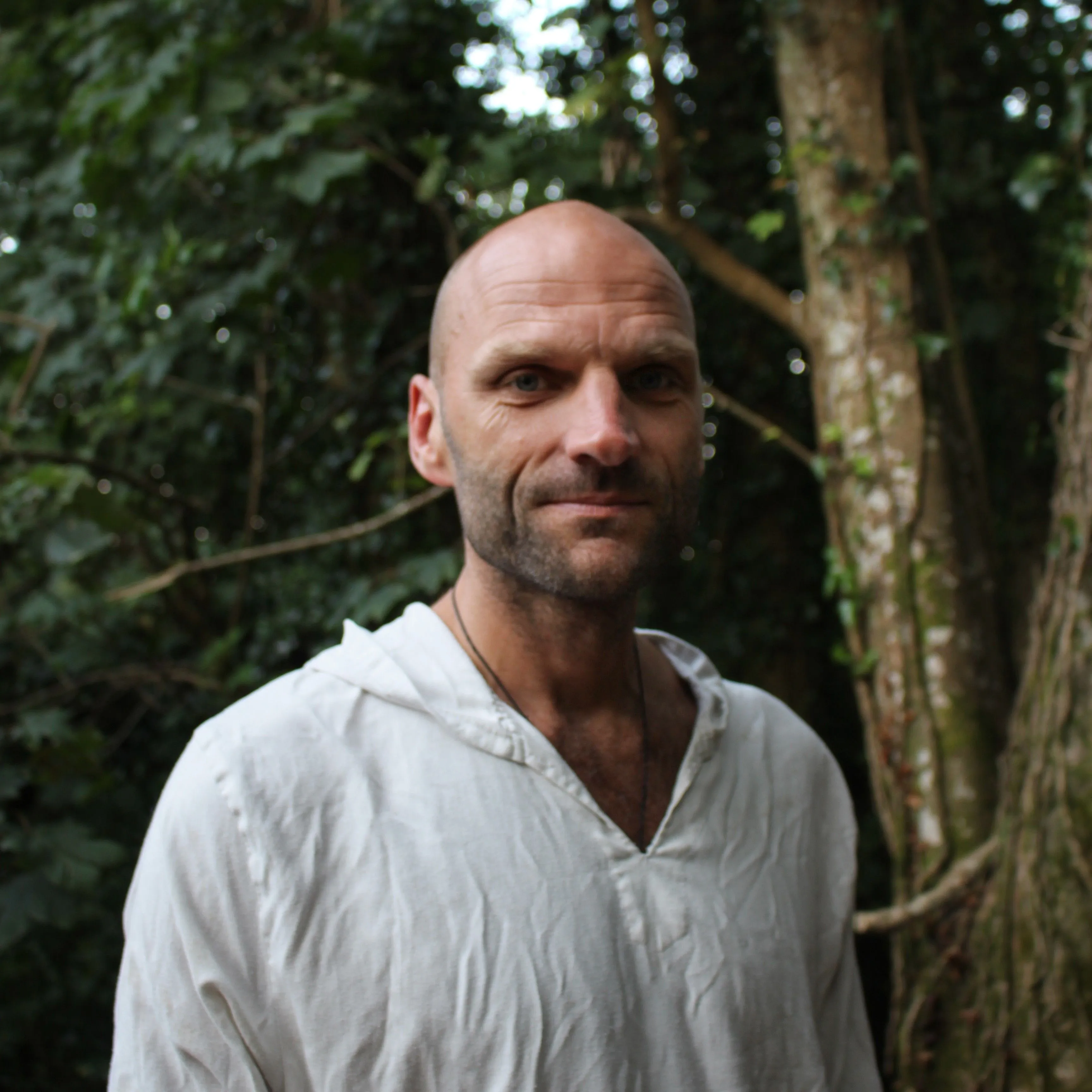Portrait of John Honeybell wearing a white shirt in a leafy forest