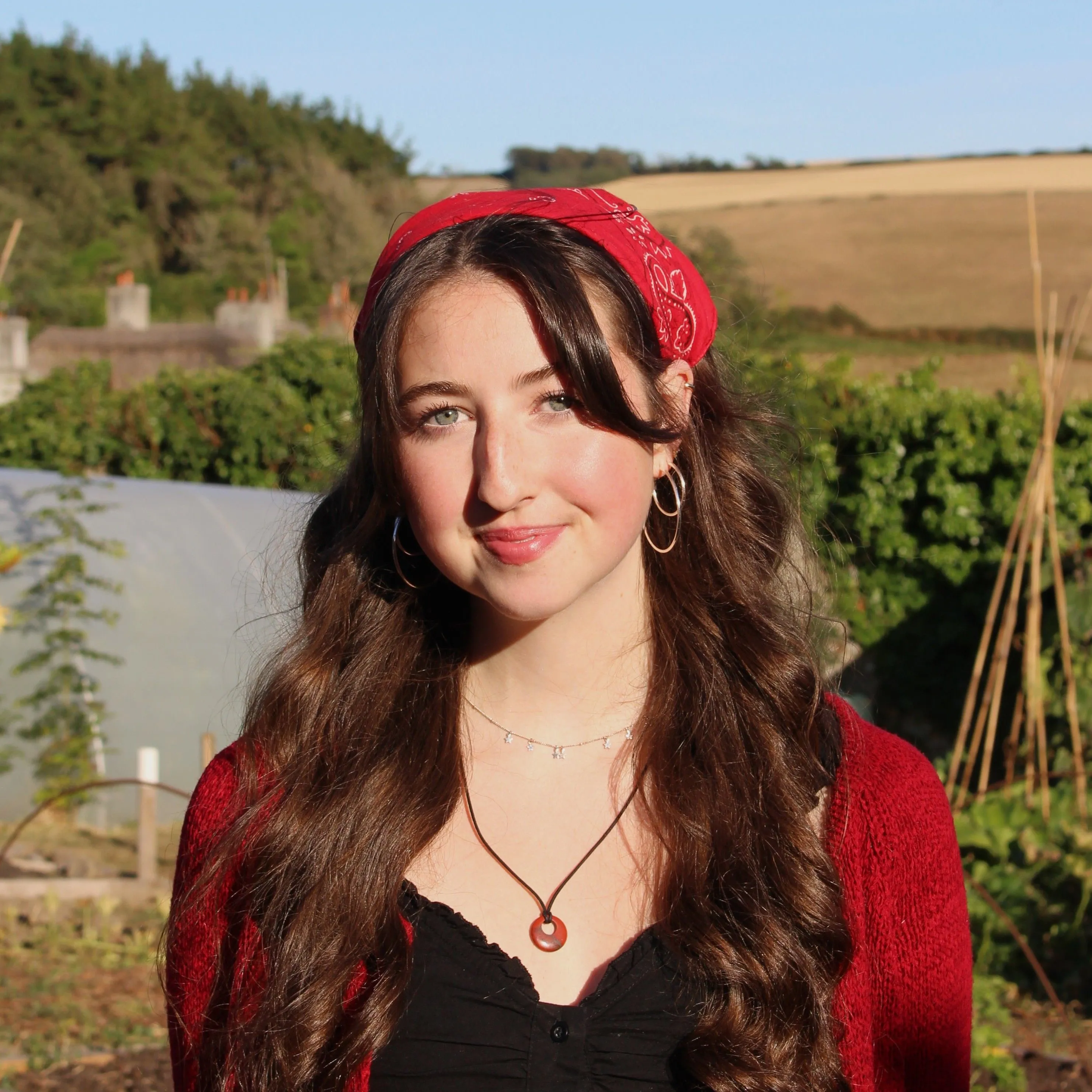 Portrait of a smiling young woman wearing a red patterned headscarf in a sunny vegetable garden.