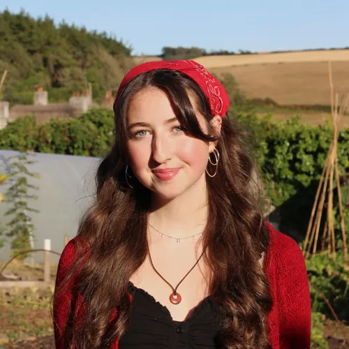 Portrait of a smiling young woman wearing a red patterned headscarf in a sunny vegetable garden.