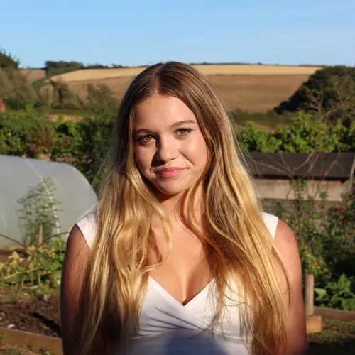 Sunlit portrait of a young woman with long blonde hair standing in a rural garden