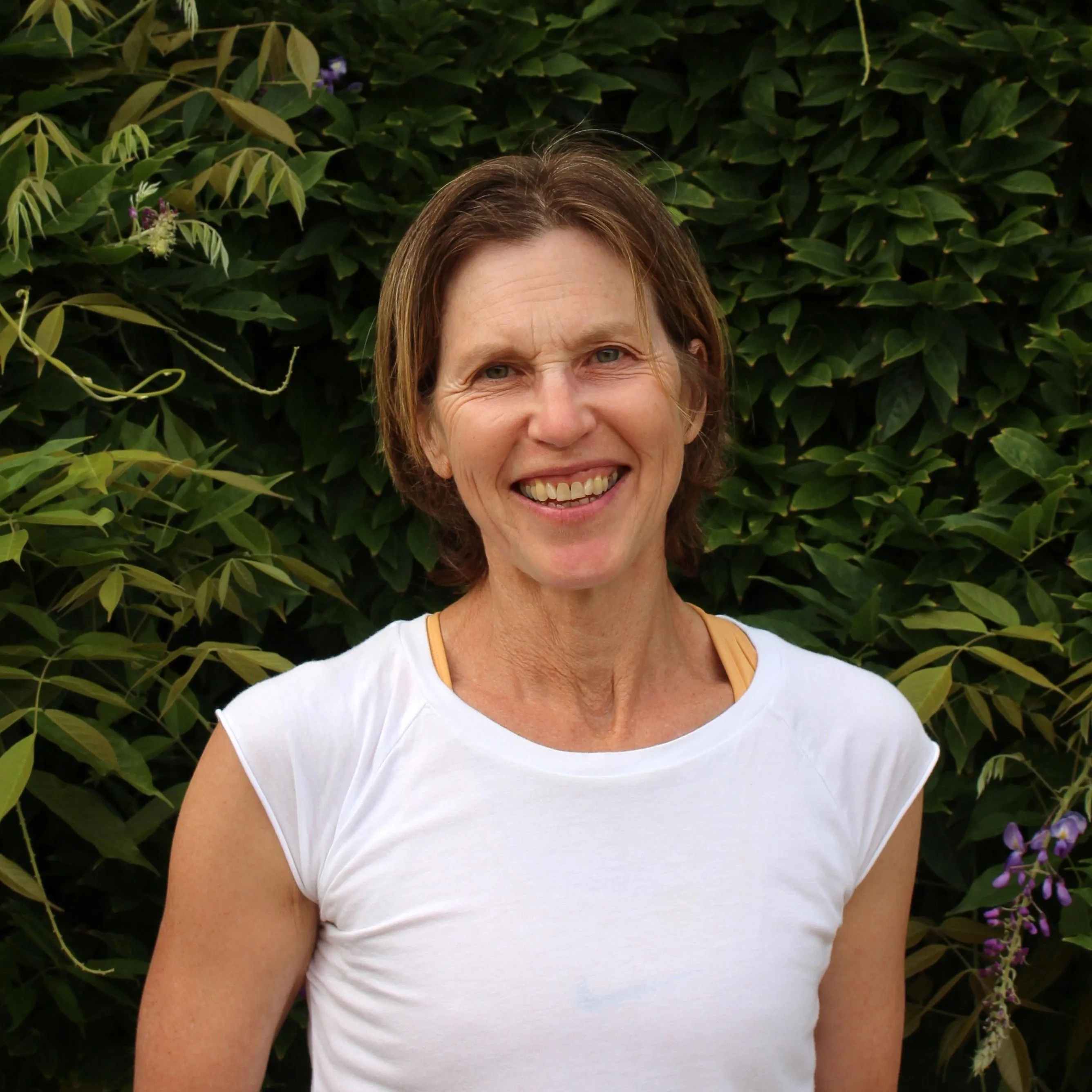 Smiling woman in a white top standing before leafy garden foliage