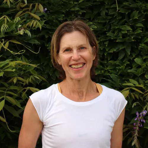 Smiling woman in a white top standing before leafy garden foliage