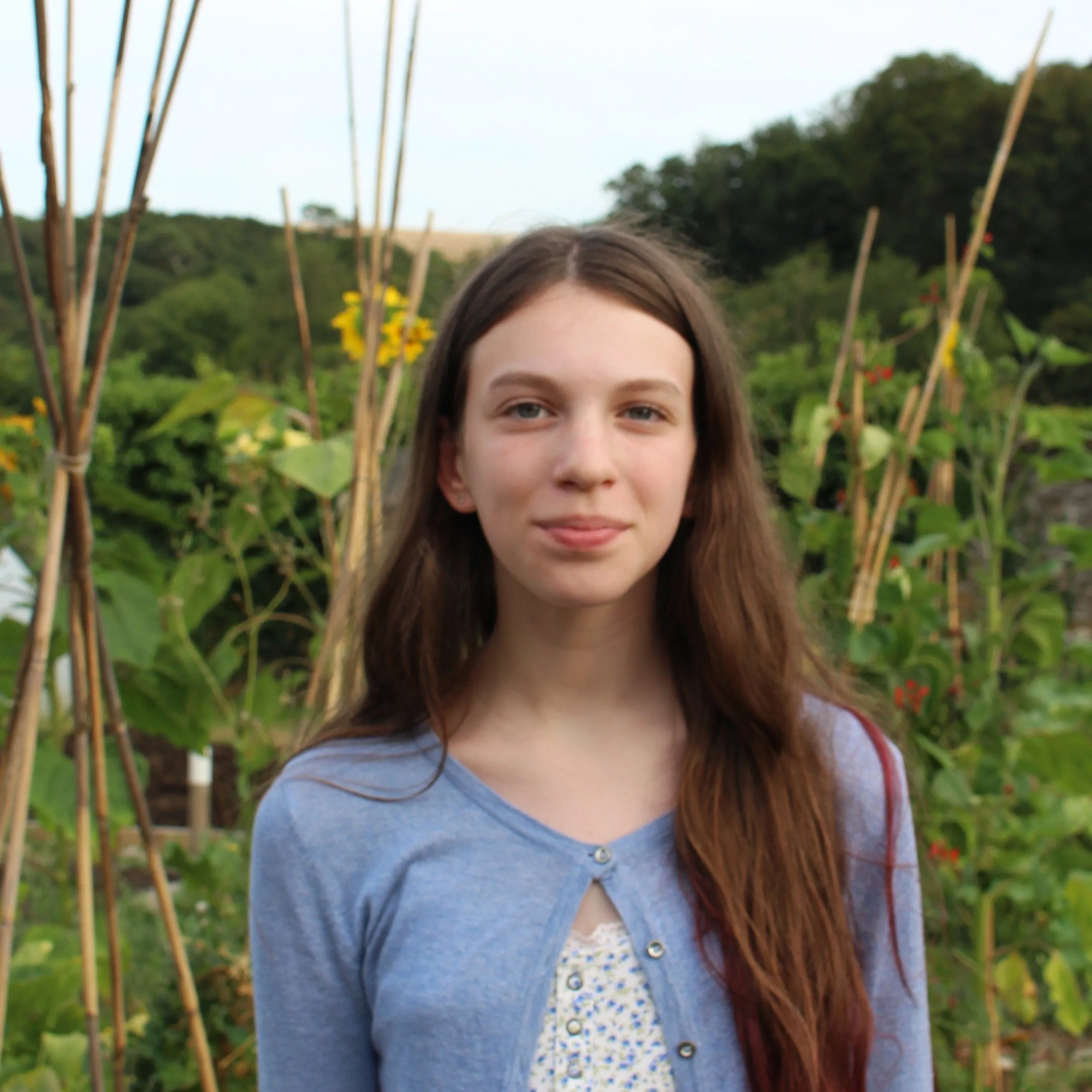 Portrait of a young girl with long brown hair standing in a leafy garden