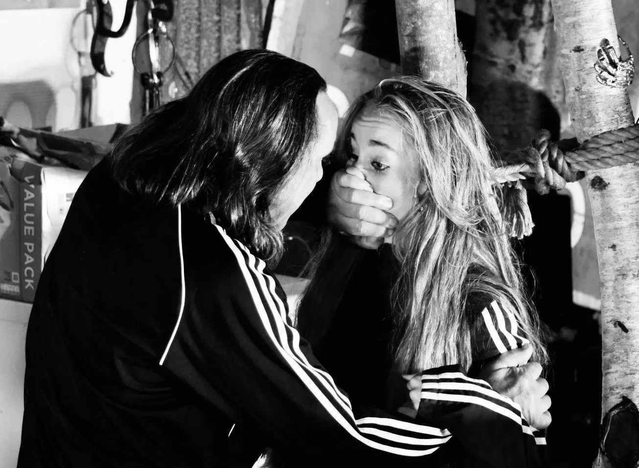 Black-and-white dramatic scene of a man restraining a frightened blonde woman in a cluttered interior