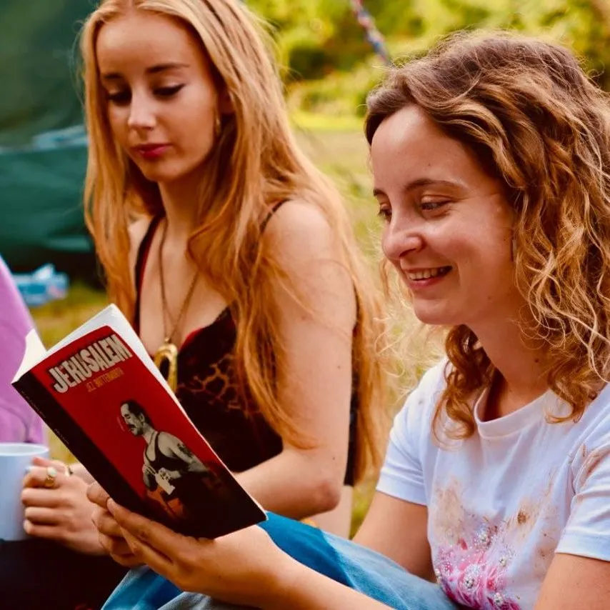 Maia Phippin smiling outdoors while holding a red book beside two women at a festival campsite.