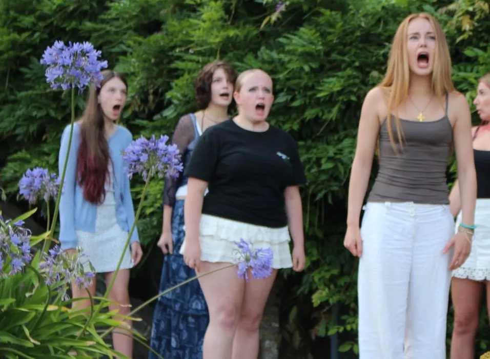 Cast members rehearse an outdoor scene from The Crucible in a flower-filled garden.