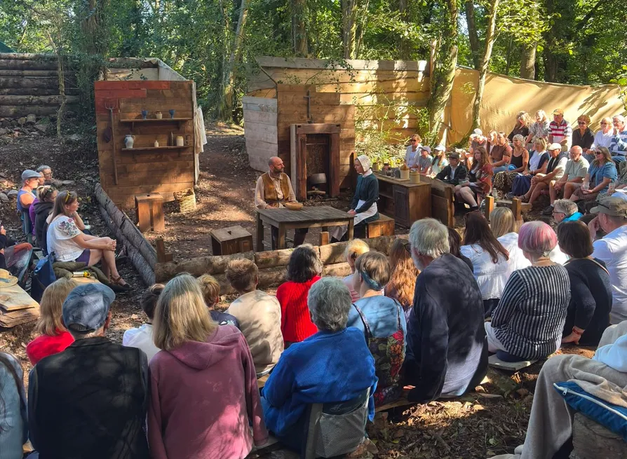 Audience watching two costumed performers in a rustic outdoor woodland theatre